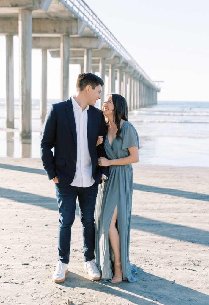 Engaged couple embracing on the sand at Scripps Pier.