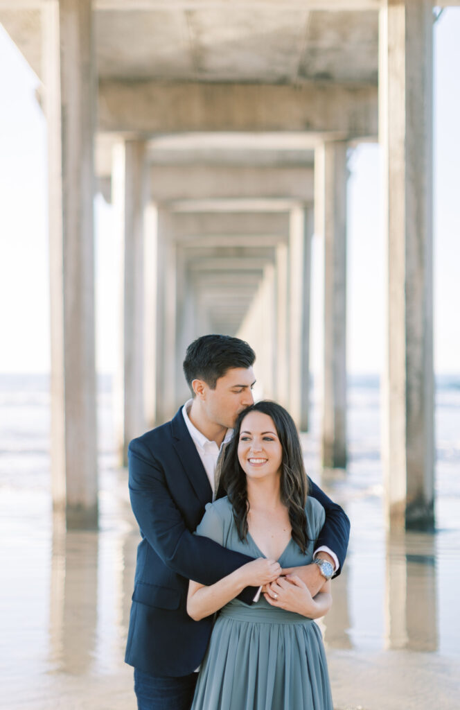 Engaged couple standing under Scripps Pier at their engagement session.