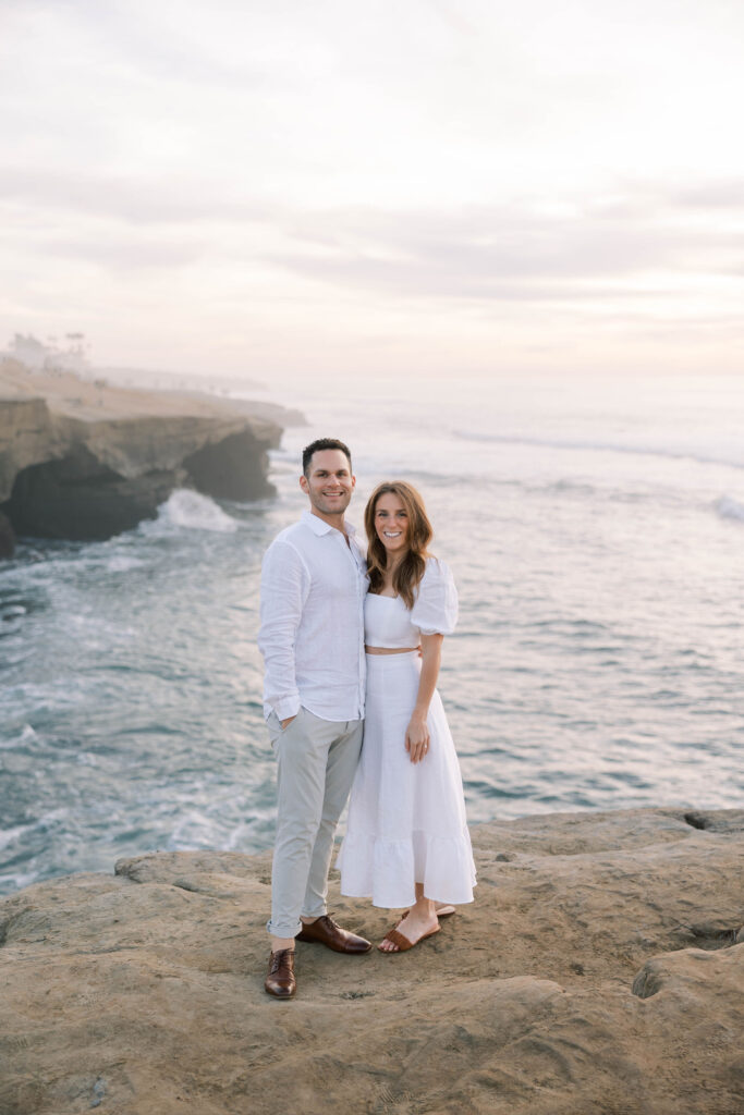 Golden hour at Sunset Cliffs, with soft light illuminating the couple and ocean below