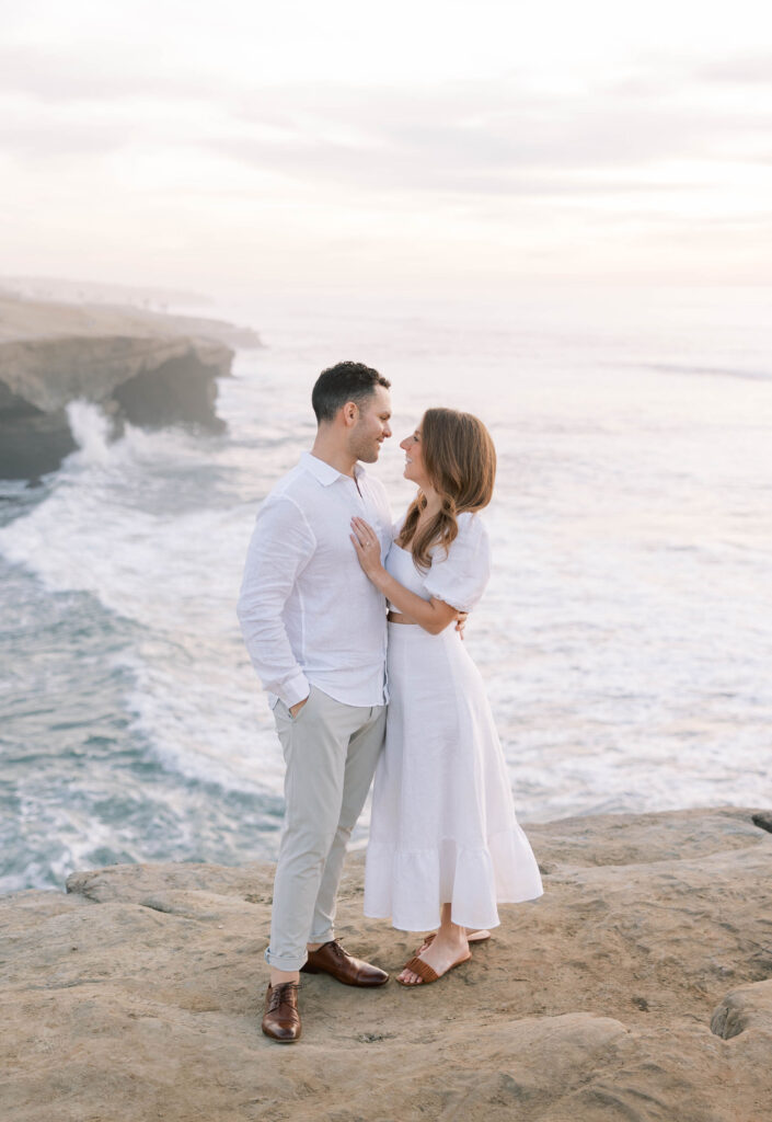 Golden hour at Sunset Cliffs, with soft light illuminating the couple and ocean below