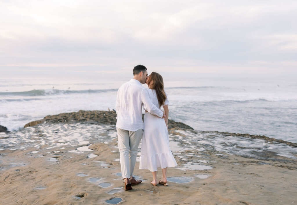 Engaged couple embracing at Sunset Cliffs in San Diego with dramatic ocean views during golden hour