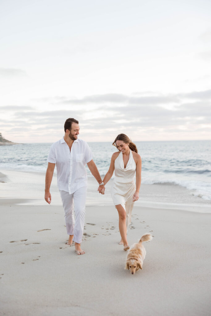 Engaged couple walk on Windansea Beach with their dog during engagement photos.