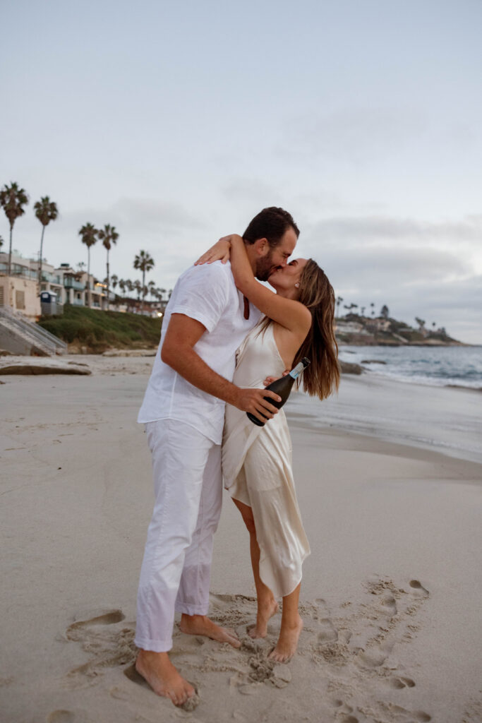 Couple kiss and hold a champagne bottle on Windansea Beach in La Jolla.