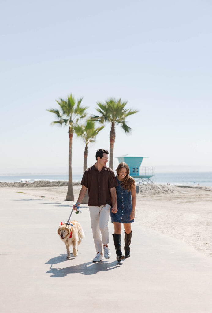Couple holding hands and walking dog at Hotel Del Coronado engagement session