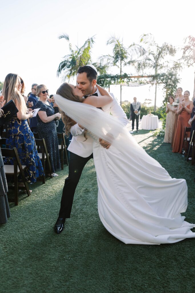 Bride and groom kiss as they walk back down the aisle after wedding ceremony at Park Hyatt Aviara