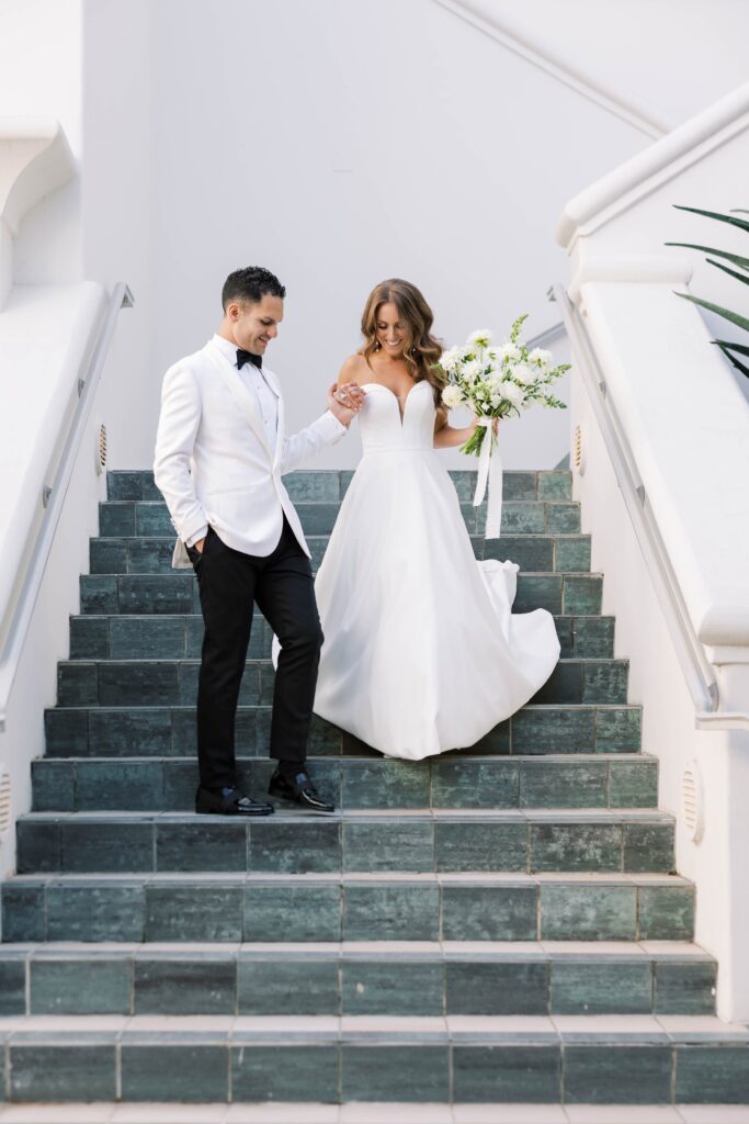 Bride and groom walking down stairs holding a bouquet in Park Hyatt Aviara